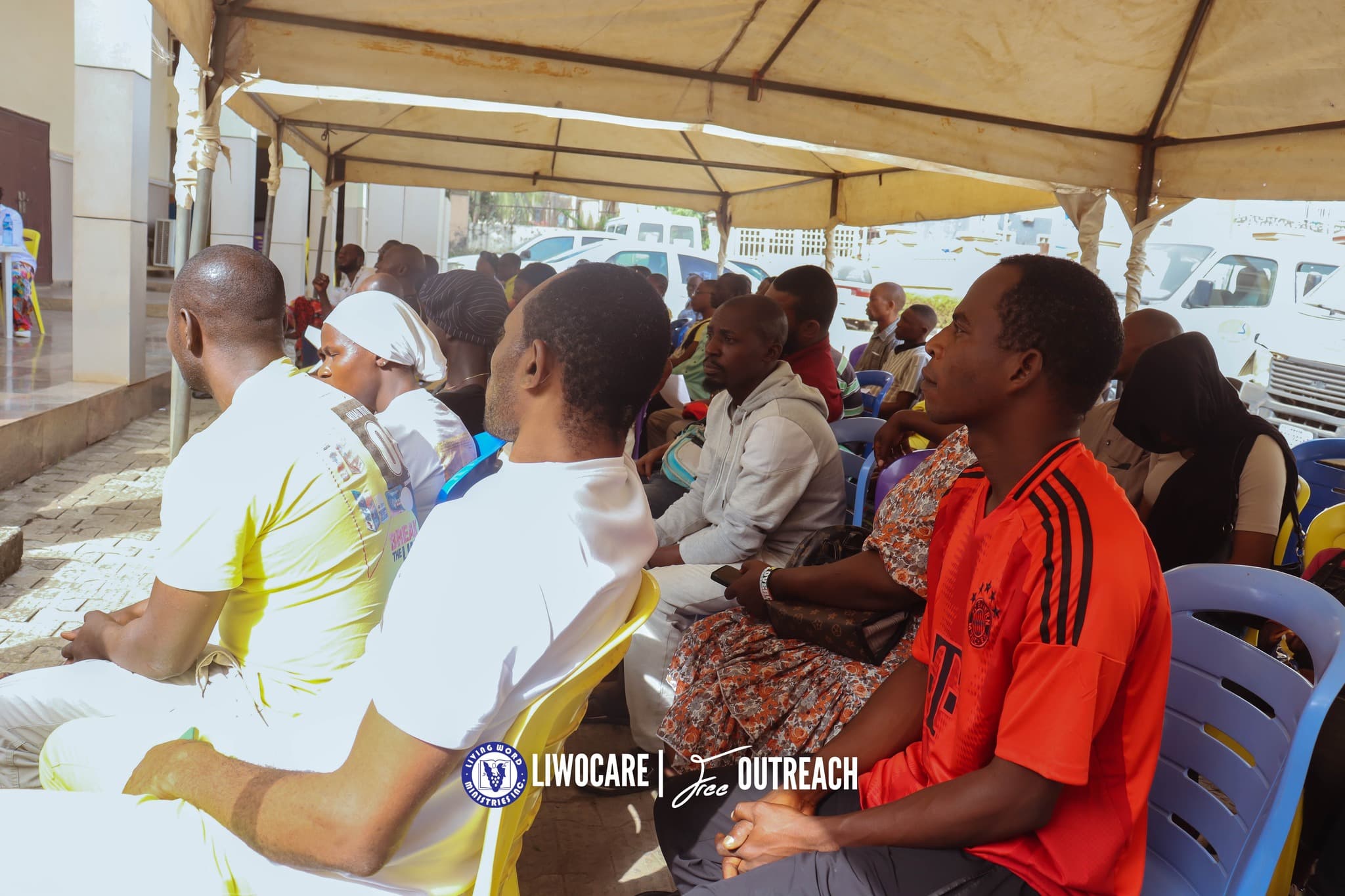 A side view of a seated audience under a large outdoor tent