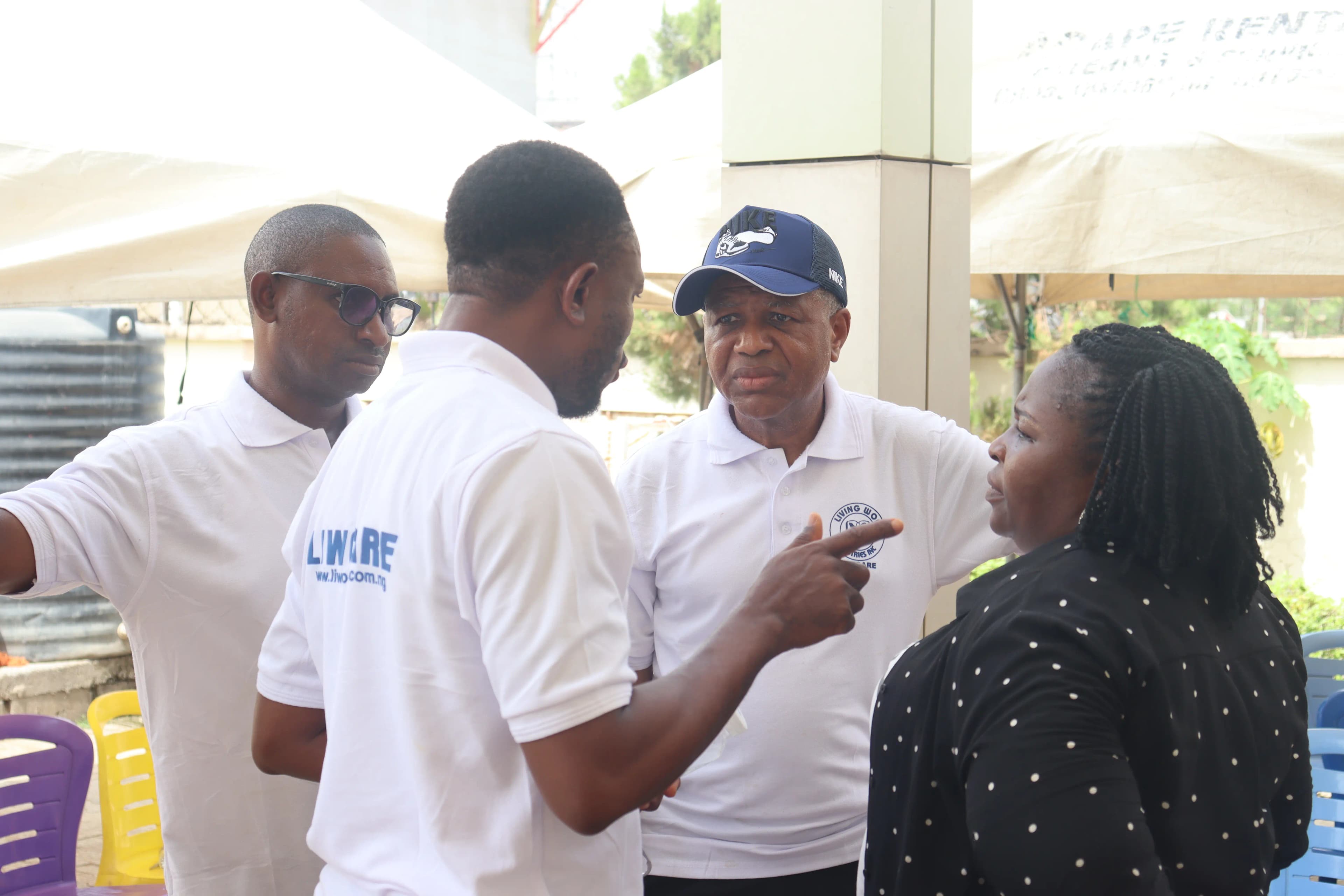 Three men in white outreach shirts and a woman in a polka-dot blouse stand outdoors engaged in a serious conversation.