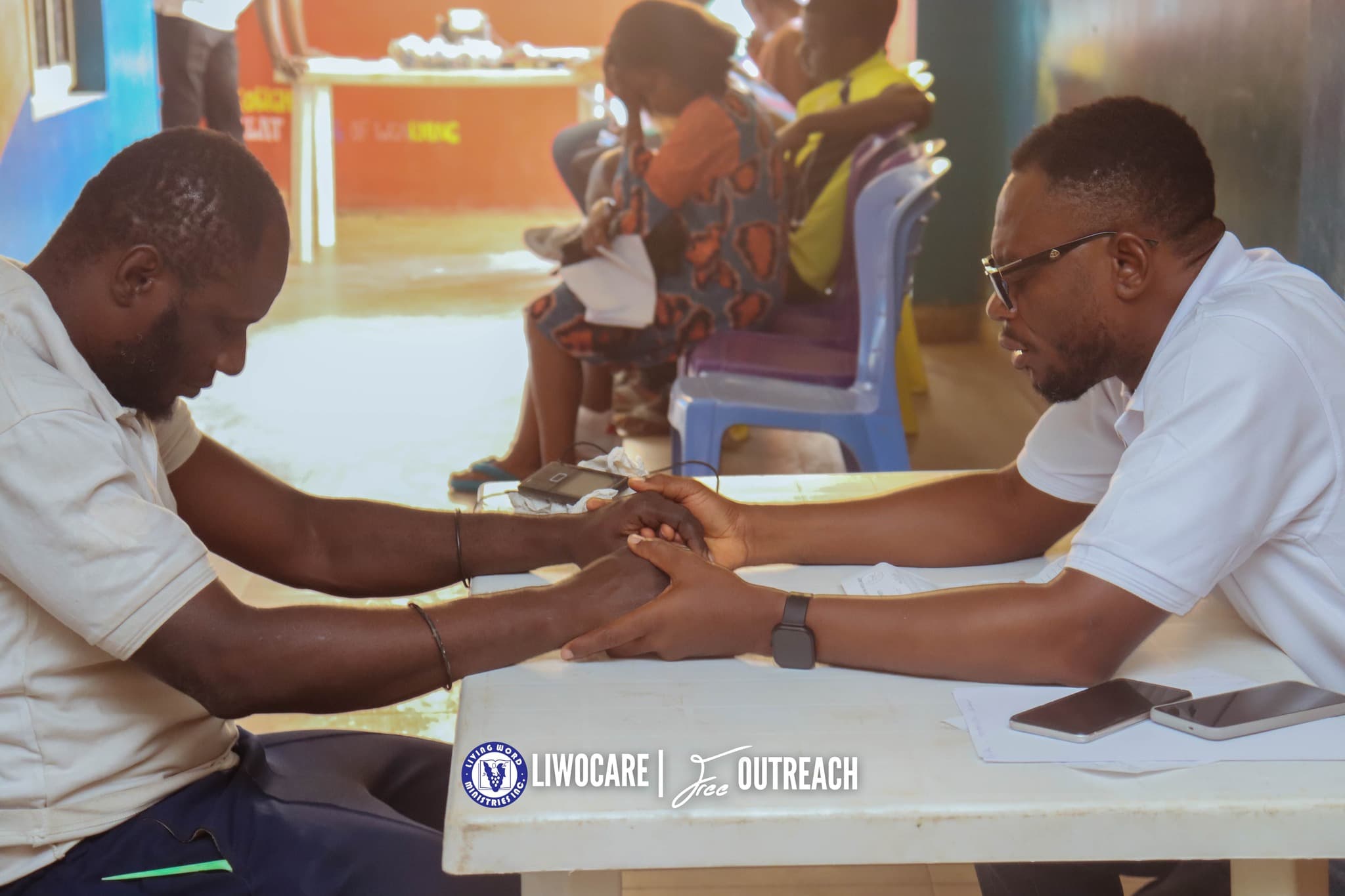 Two men witting across from each other at a table holding hands in prayer with their eyes closed